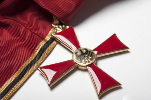 Foto des Bundesverdienstkreuzes (ein rotes Kreuz an einem goldenen Band)