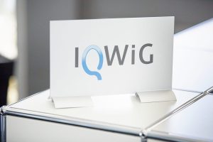 Schild mit Schriftzug "IQWIG" steht auf einem Tresen.