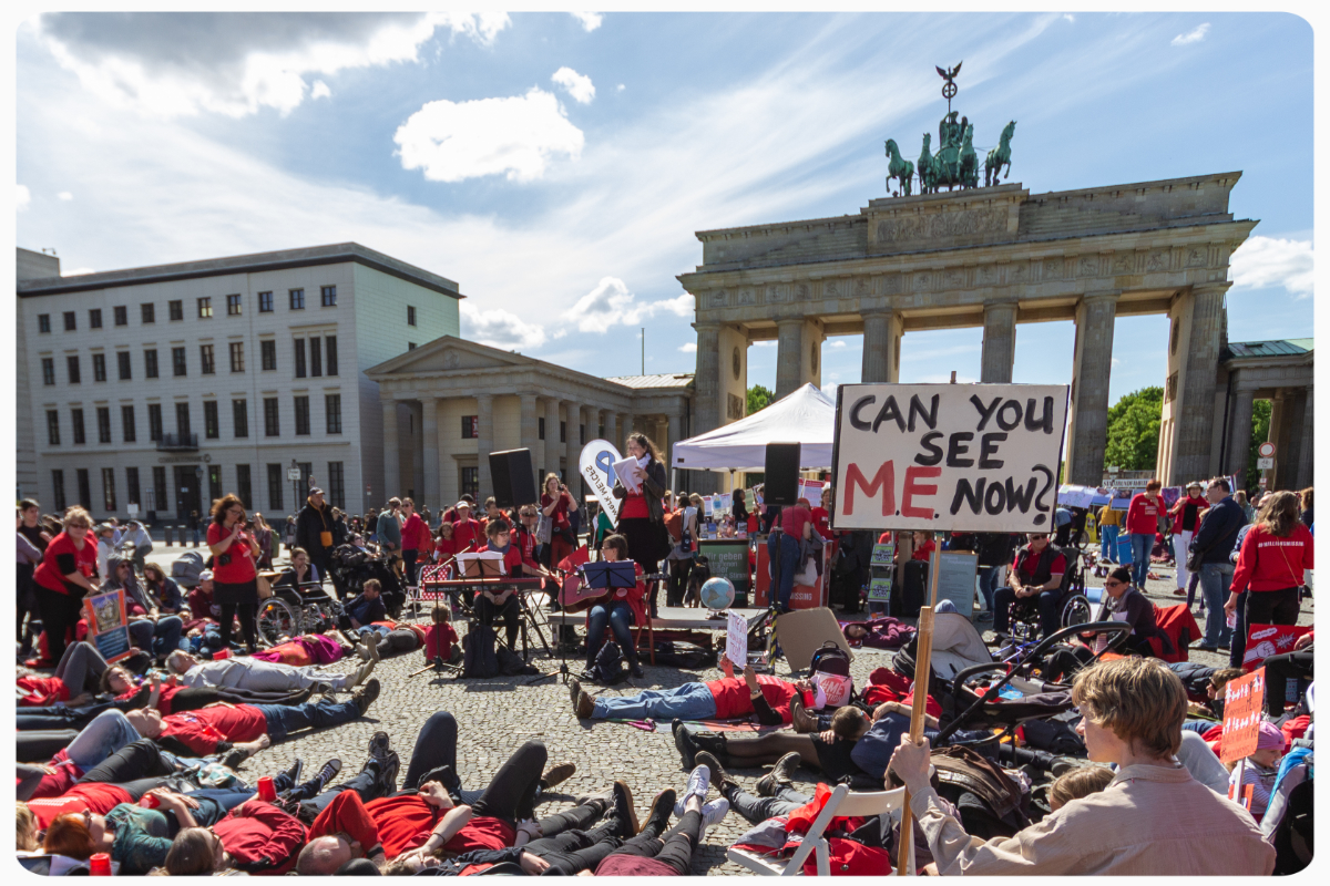 Foto der Demo von #MillionsMissing Deutschland und der Deutschen Gesellschaft für ME/CFS am 12. Mai 2019 vor dem Brandenburger Tor. Eine Gruppe Menschen ist zu sehen, manche liegen auf dem Boden, einige haben Schilder, auf einem steht "Can you see ME now?".