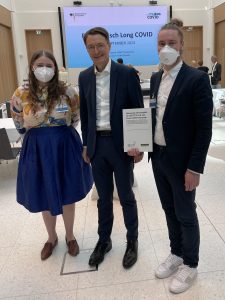Gesundheitsminister Lauterbach steht mit Mia Diekow von Long COVID Deutschland und Sebastian Musch von der Deutschen Gesellschaft für ME/CFS zusammen.