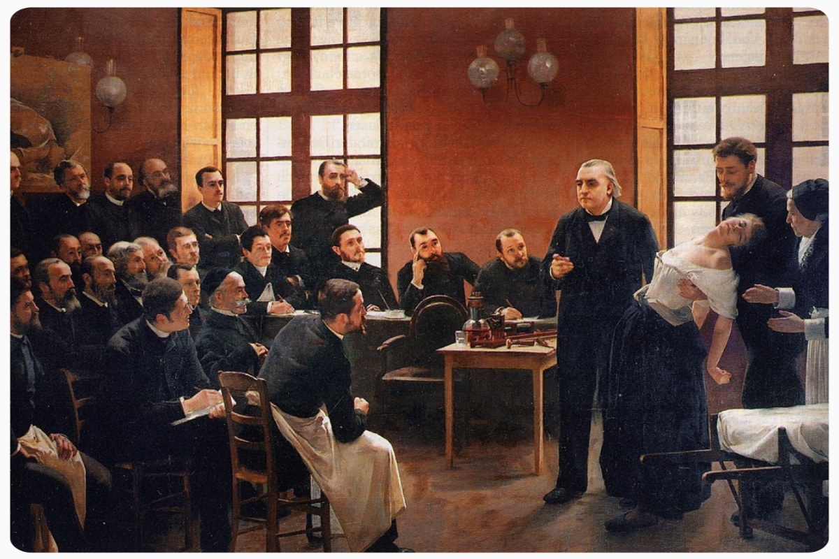 Das Bild zeigt das Gemälde "Eine klinische Lektion in der Salpêtrière", ein Tableau-Gruppenbildnis aus dem Jahr 1887. Zu sehen ist ein Neurologe, der einer Gruppe von Studenten eine klinische Demonstration mit einer Patientin gibt.